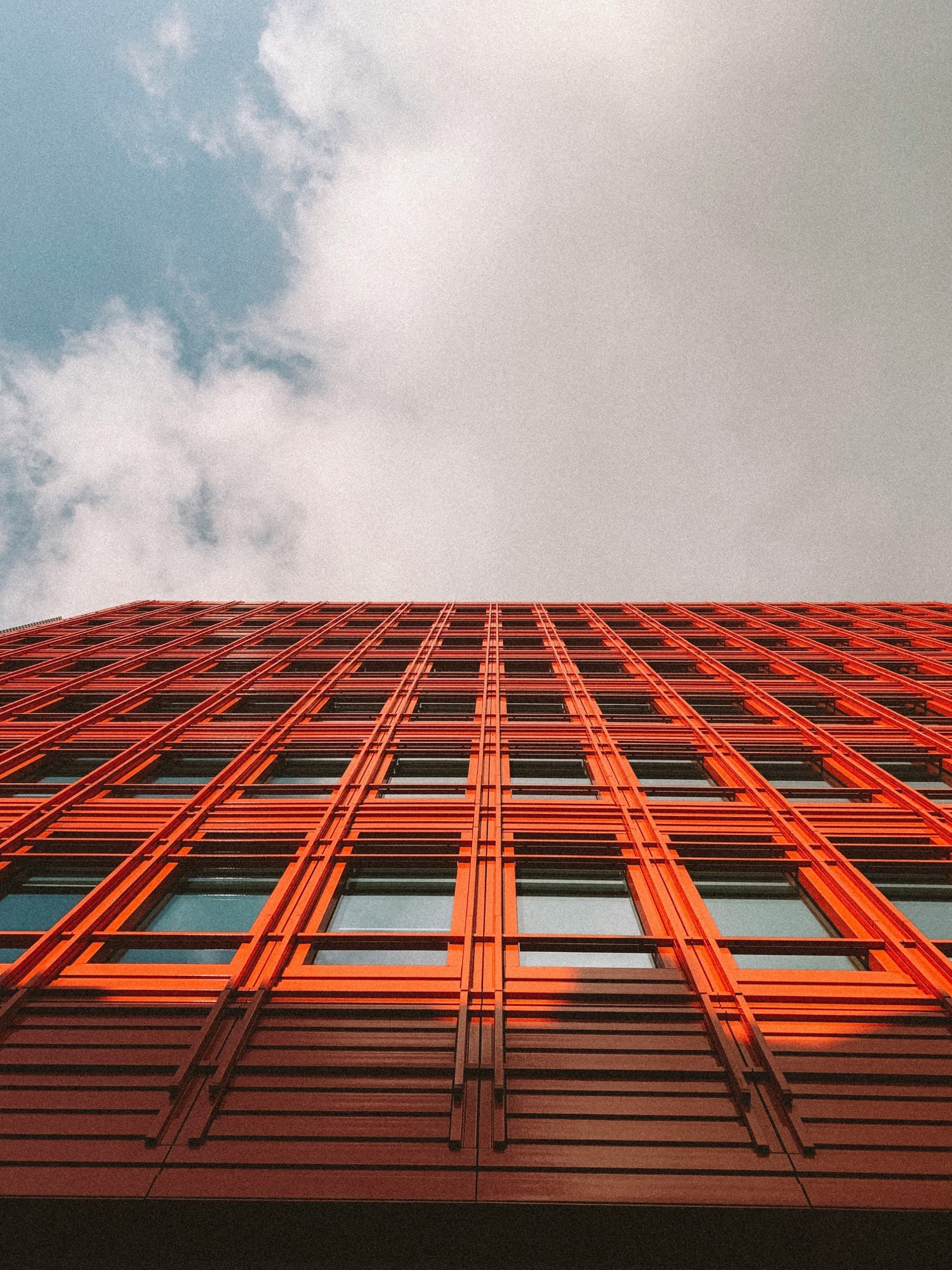 Looking up at a bold orange gridded building facade against the sky